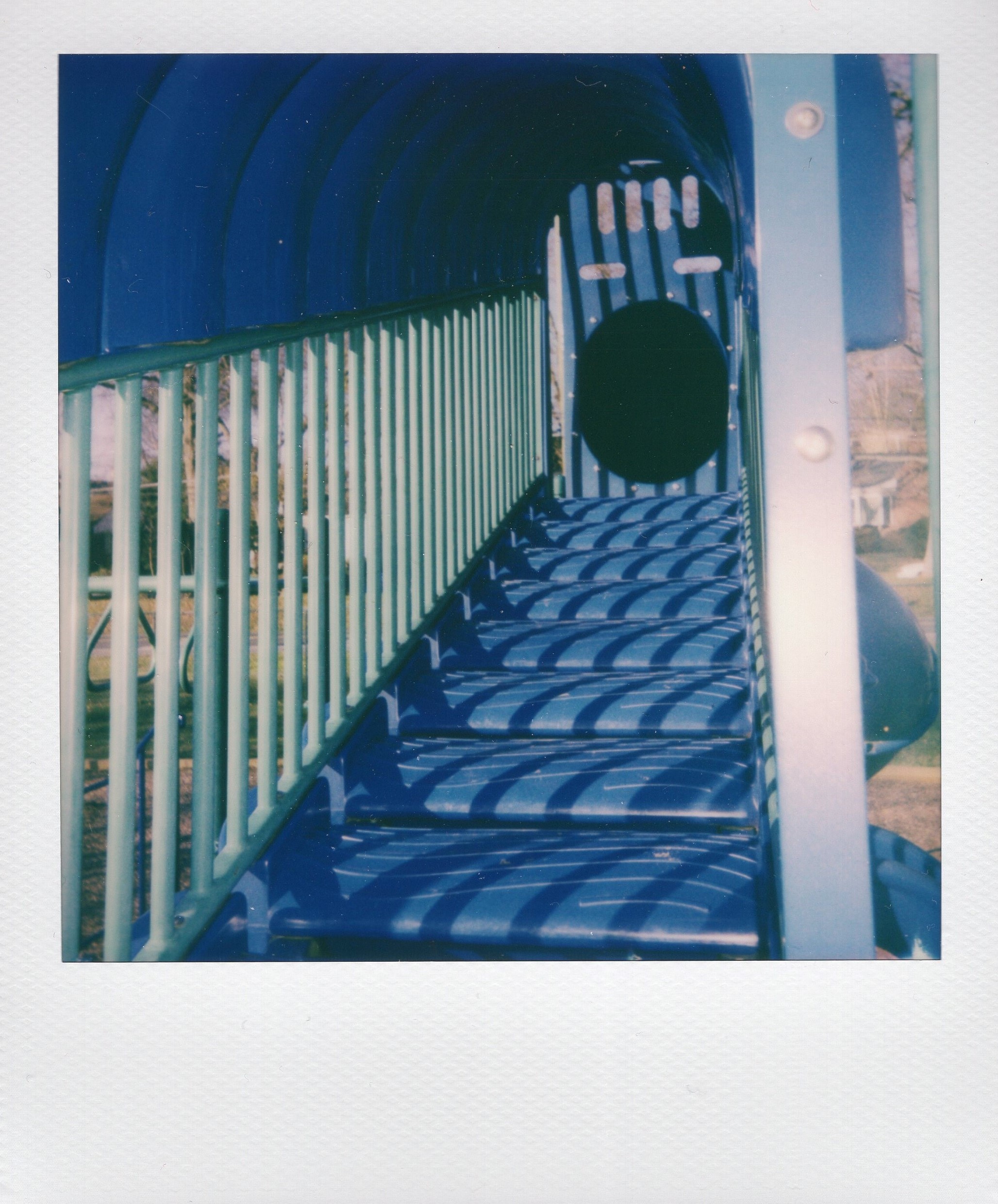 Color Polaroid of blue stairs and a tunnel that are part of playground equipment